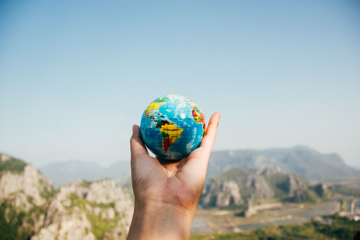 Hand holding a small globe with green mountains and pale blue sky in the background